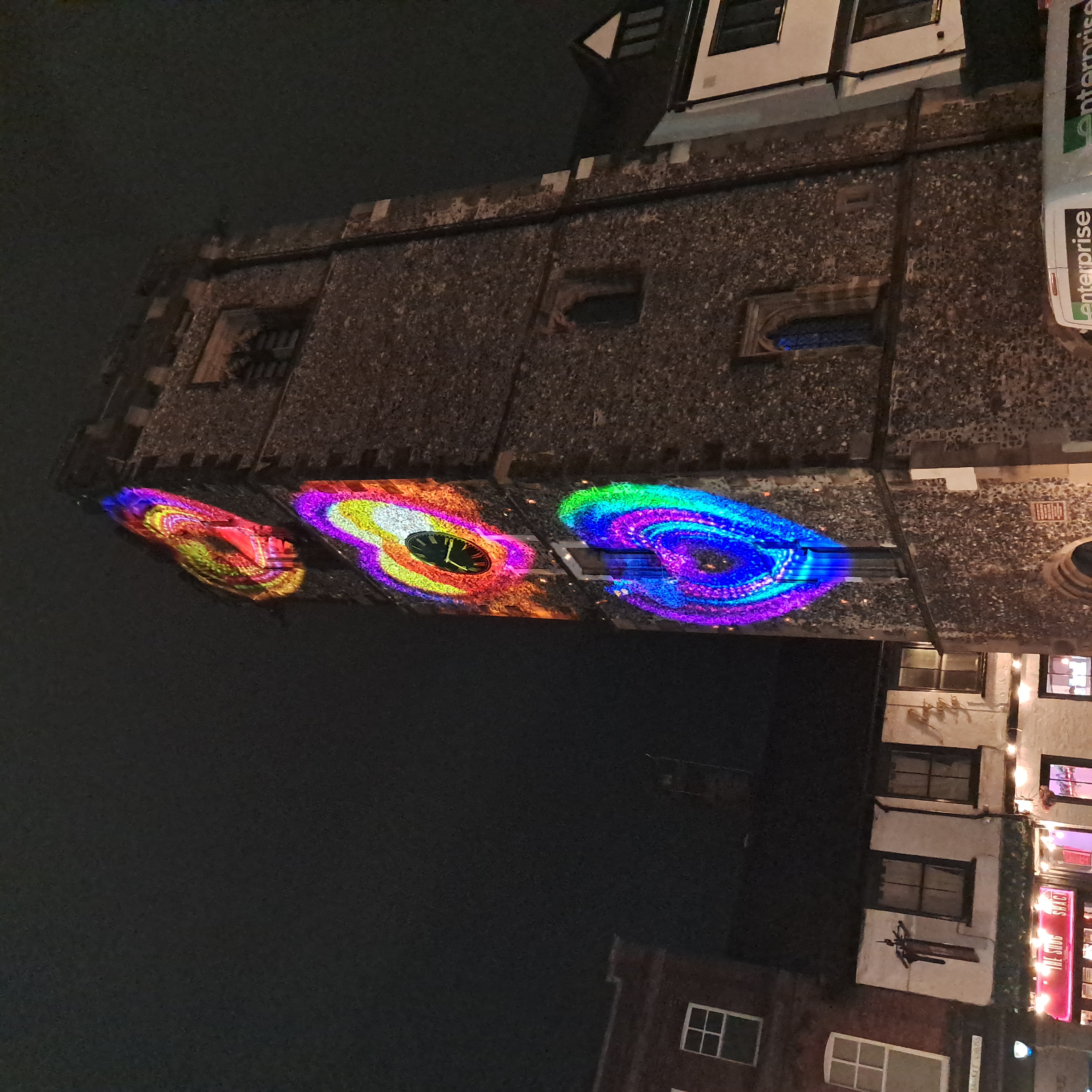 St Albans Clock Tower illuminated with vivid projected hearts at night, bringing colour to the medieval landmark and surrounding city centre street.